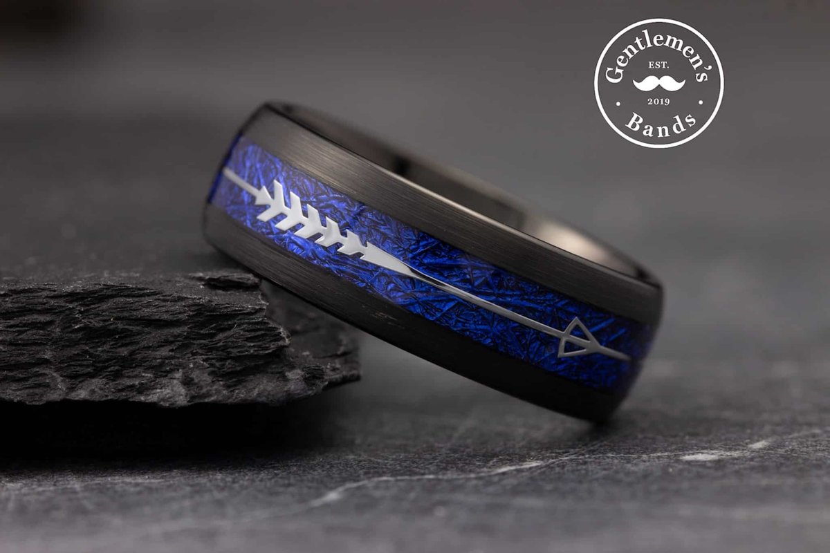 The Archer, a black tungsten carbide ring with a brushed finish that features a blue meteorite inlay with a silver feathered arrow.