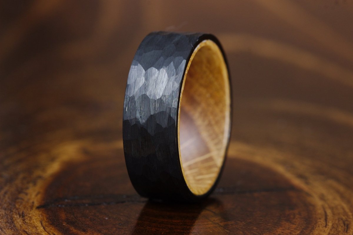 The Outlaw, a black tungsten carbide wedding band that features a hammered and brushed finish and a whiskey barrel wood band.